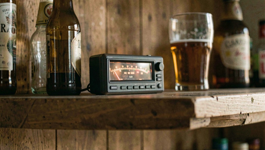 A corner stage in a small bar at dusk, two guitar amps angled across the boards, a single vocal mic under a low ceiling, warm tungsten light from the bar behind the empty floor.